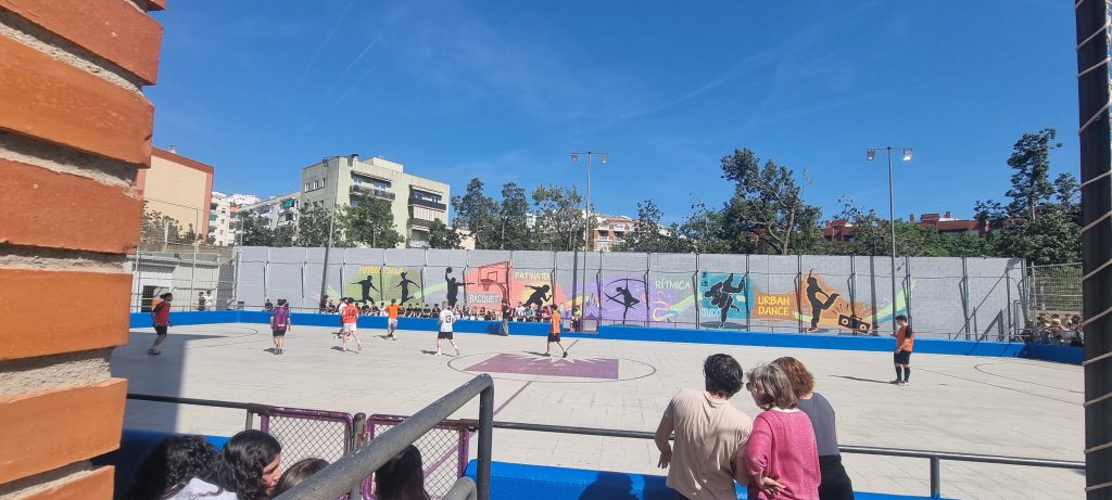 Mural en escuela del clot siluetas de personas en pared y deportes con niños jugando adelante